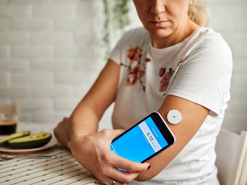 A woman using a remote patient monitoring device to monitor her blood sugar.