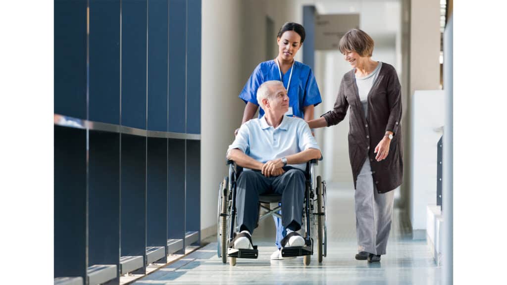 Male-in-a-wheelchair-with-a-nurse-and-woman-beside-him-as-he-is-being-discharged-from-the-hospital.