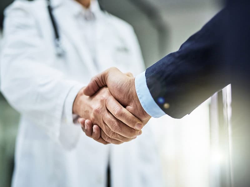 A physician and healthcare executive shaking hands, representing value-based contracting.